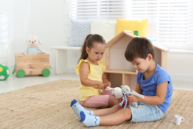 Photo of Cute little children playing with toys near wooden house on floor at home, space for text