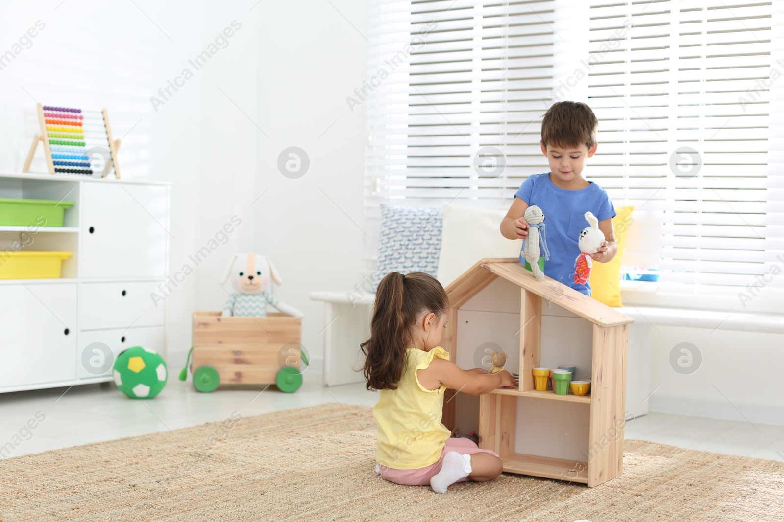 Photo of Cute little children playing with toys near wooden house on floor at home, space for text