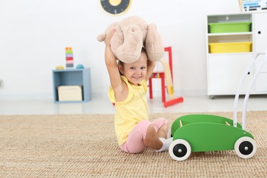 Photo of Cute little girl playing with teddy bear on floor at home. Soft toy