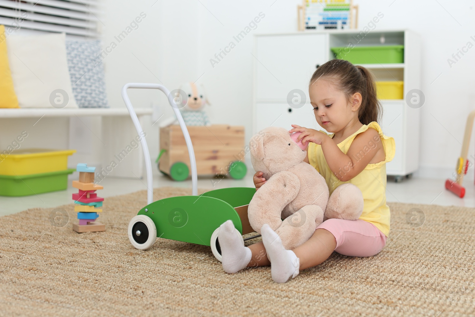 Photo of Cute little girl playing with teddy bear on floor at home. Soft toy