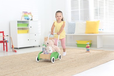 Photo of Cute little girl playing with toy walker at home
