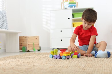 Photo of Cute little boy playing with colorful toys on floor at home, space for text