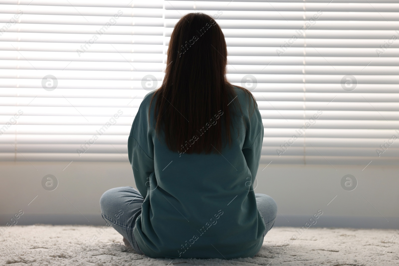 Photo of Loneliness concept. Sad woman sitting on floor at home, back view