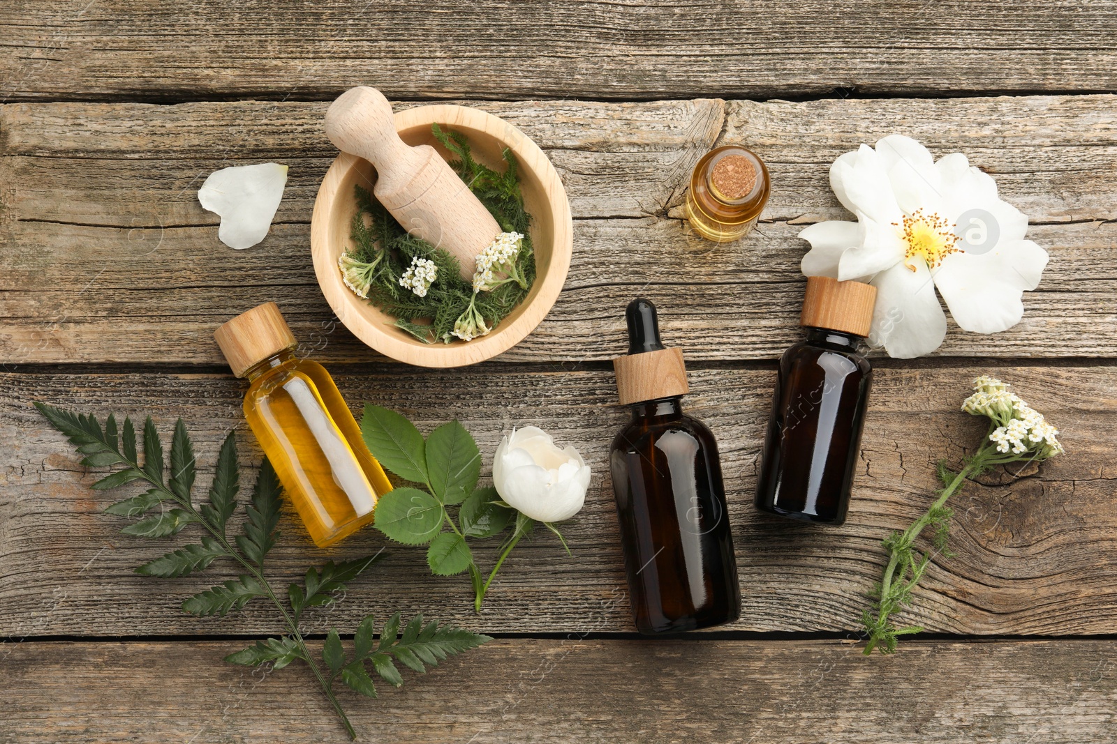 Photo of Aromatherapy. Different essential oils, flowers, green leaves, mortar and pestle on wooden table, flat lay