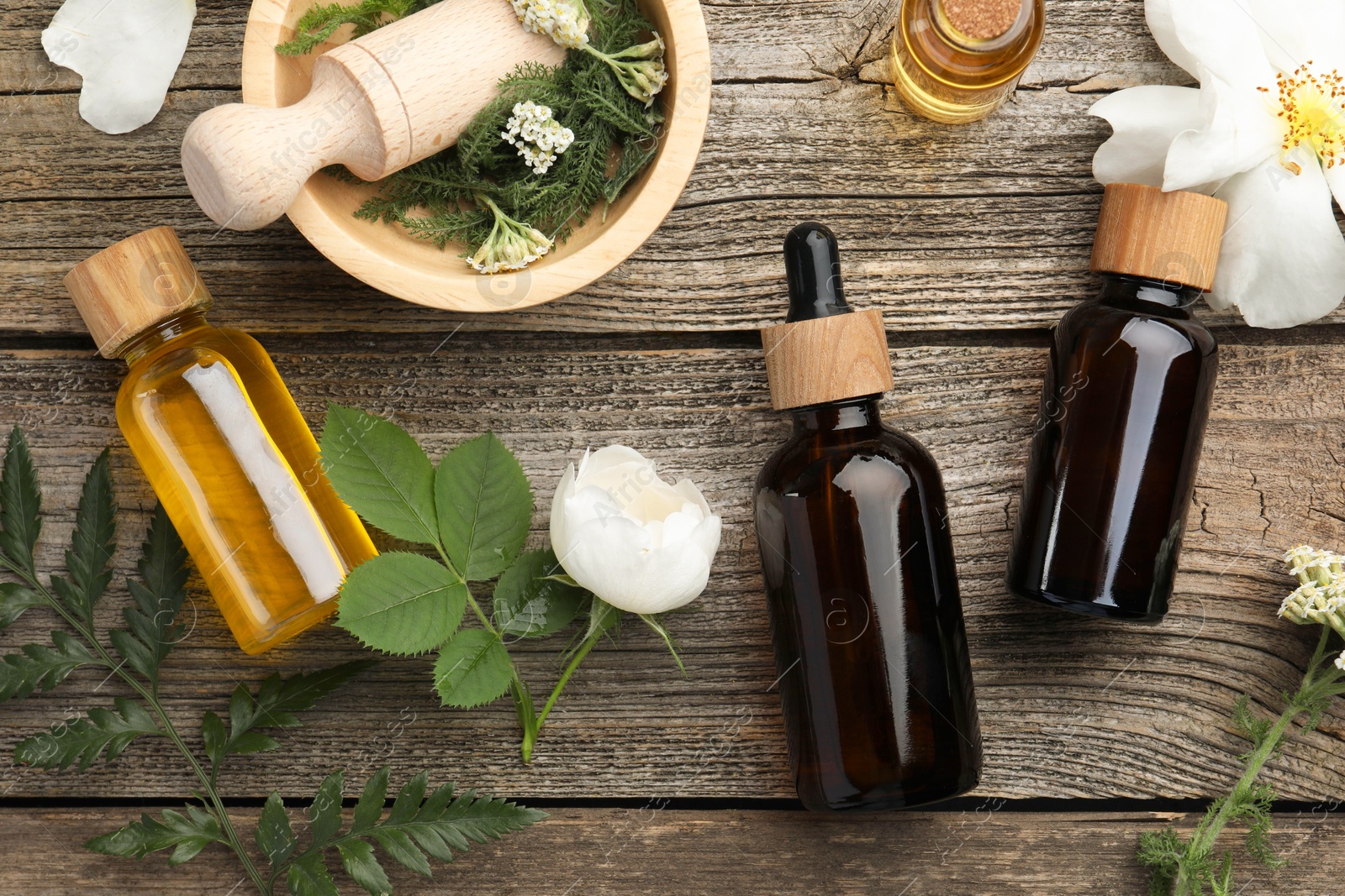 Photo of Aromatherapy. Different essential oils, flowers, green leaves, mortar and pestle on wooden table, flat lay