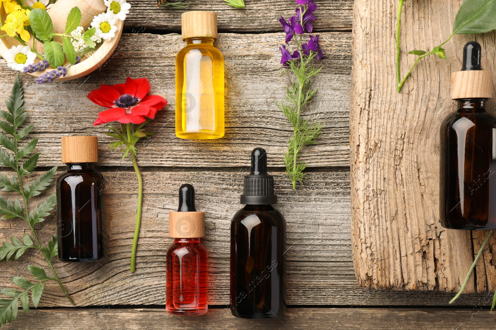 Photo of Aromatherapy. Different essential oils and flowers on wooden table, flat lay