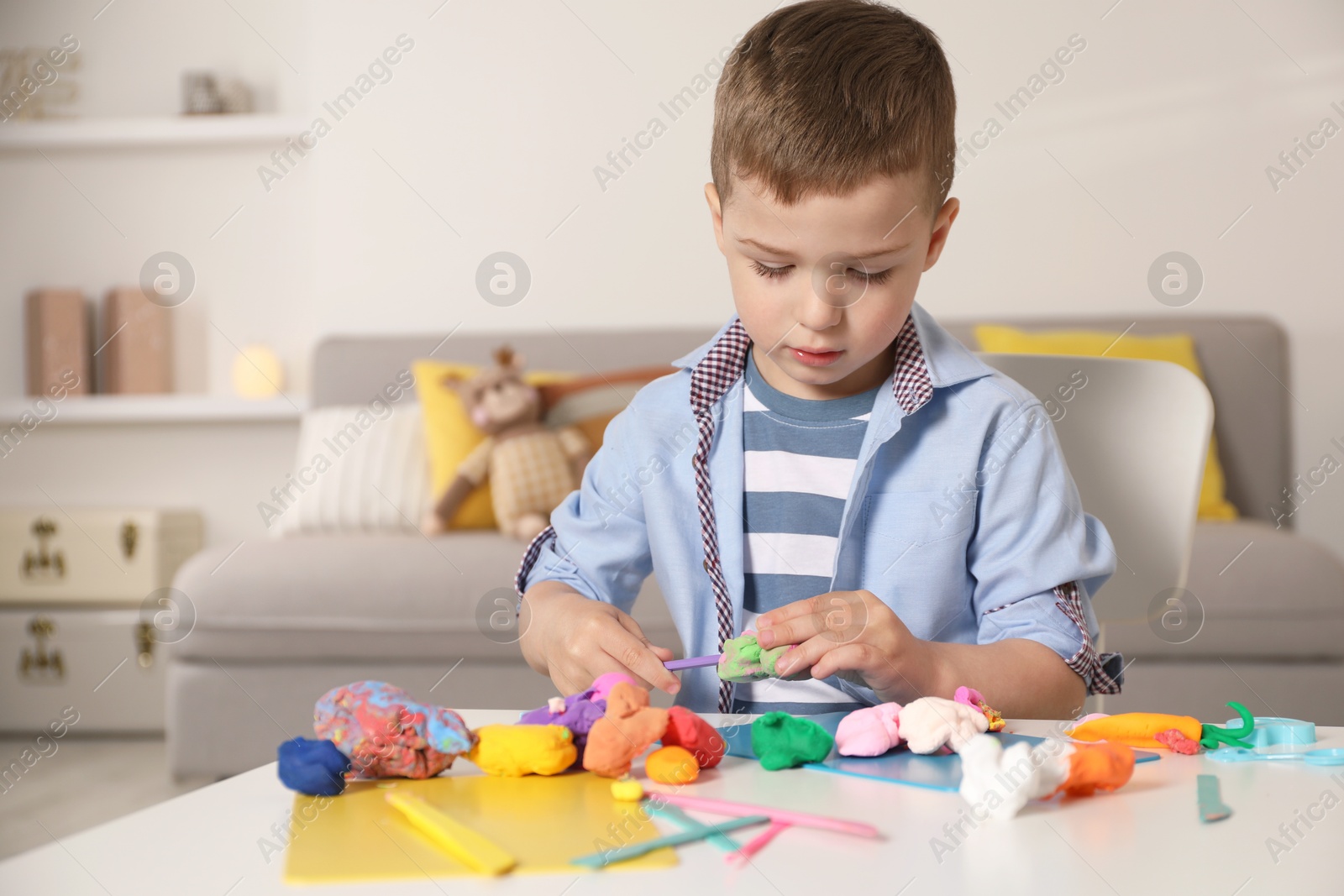 Photo of Little boy sculpting with play dough at table in kindergarten