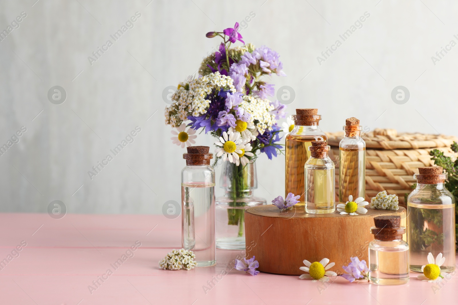 Photo of Aromatherapy. Different essential oils and flowers on pink wooden table, space for text