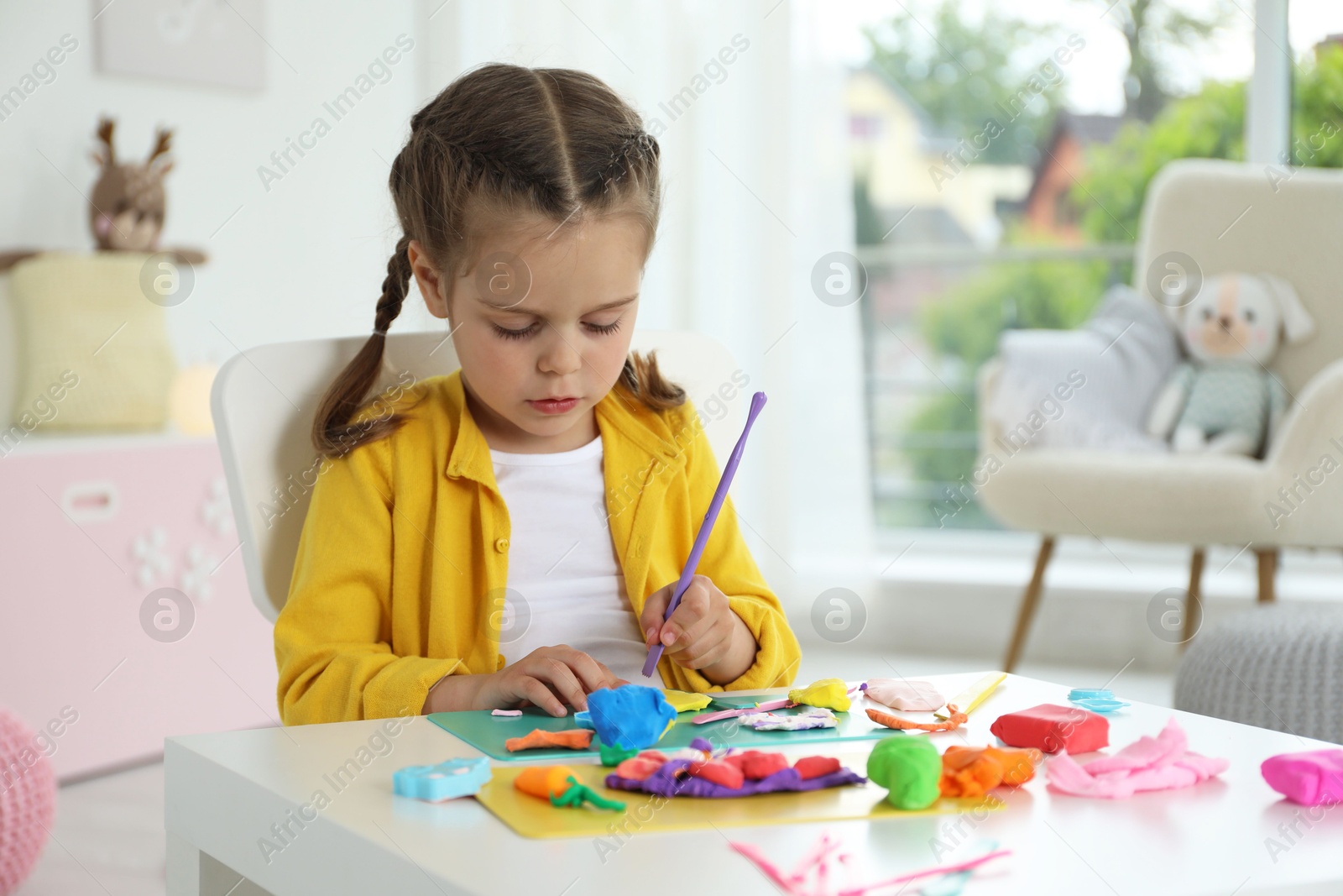 Photo of Little girl sculpting with play dough at table in kindergarten