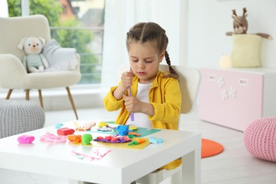 Little girl sculpting with play dough at table in kindergarten