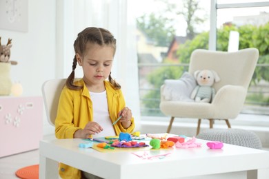 Little girl sculpting with play dough at table in kindergarten