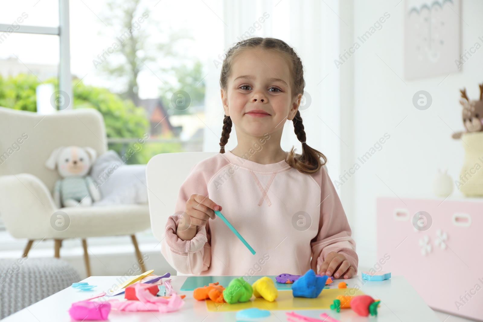 Photo of Little girl sculpting with play dough at table in kindergarten