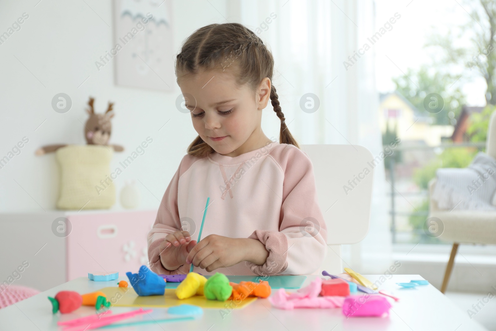 Photo of Little girl sculpting with play dough at table in kindergarten