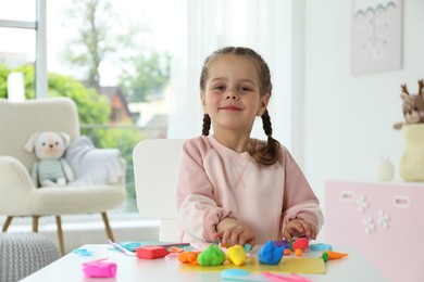 Photo of Little girl sculpting with play dough at table in kindergarten