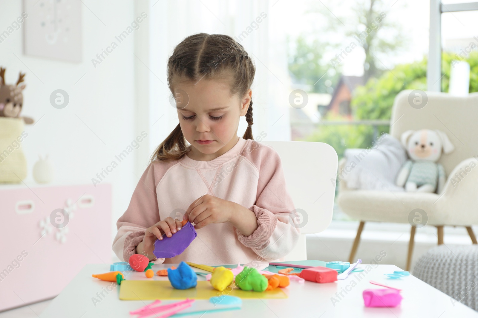 Photo of Little girl sculpting with play dough at table in kindergarten