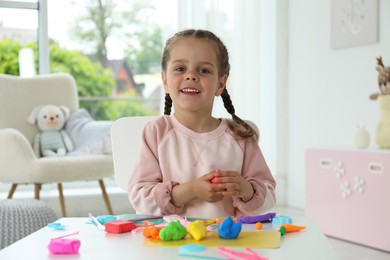 Photo of Smiling girl sculpting with play dough at table in kindergarten