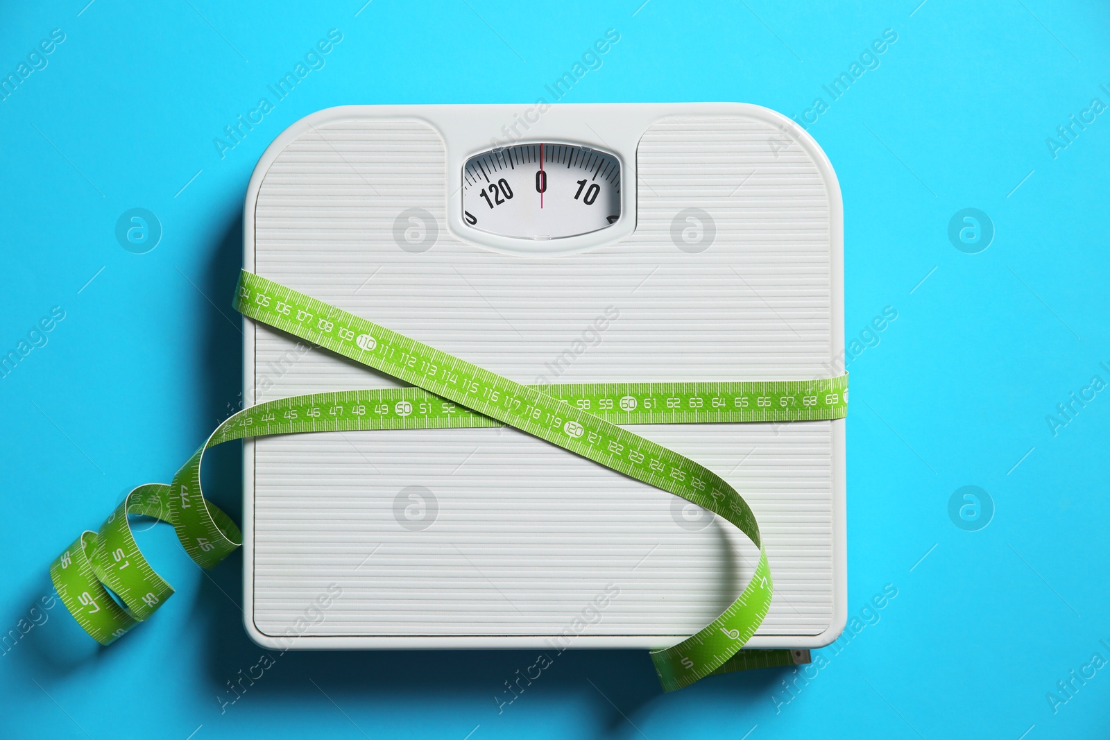 Photo of Scale tied with measuring tape on light blue background, top view