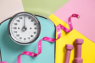 Photo of Scale, dumbbells and measuring tape on color background, flat lay