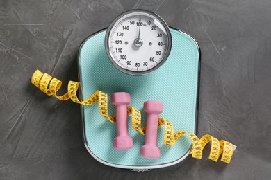 Photo of Scale, measuring tape and dumbbells on grey textured background, top view