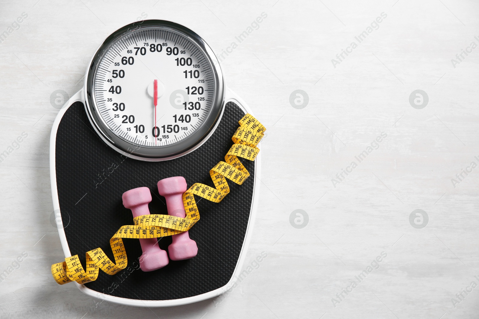 Photo of Scale, dumbbells and measuring tape on white wooden background, top view. Space for text