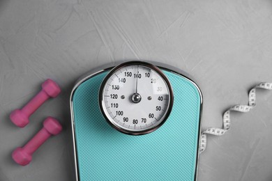 Photo of Bathroom scale, measuring tape and dumbbells on grey textured background, flat lay