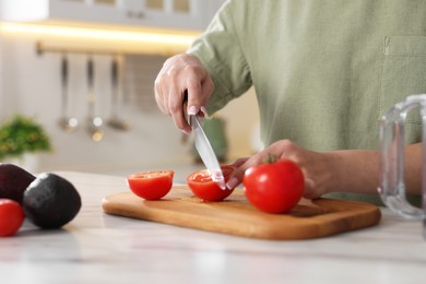 Woman cutting fresh tomato at white marble table in kitchen, closeup