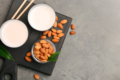 Glasses of almond milk and almonds on grey table, top view. Space for text