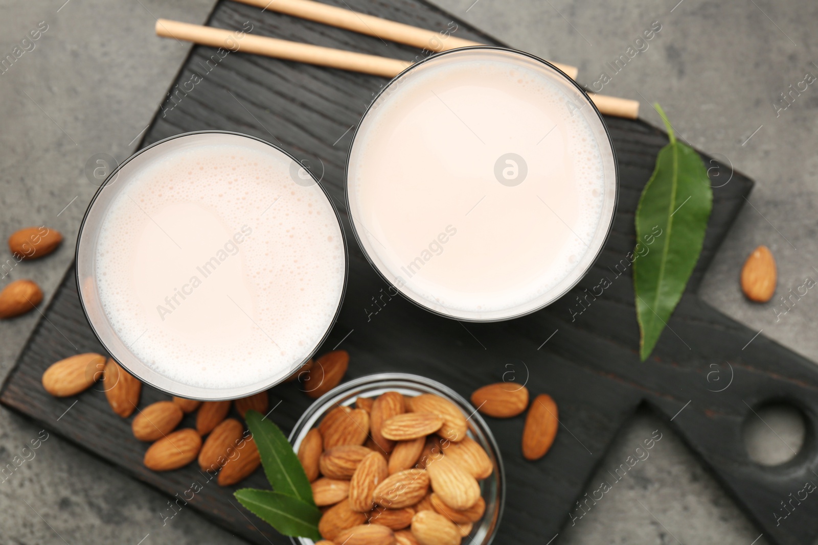 Photo of Glasses of almond milk and almonds on grey table, top view