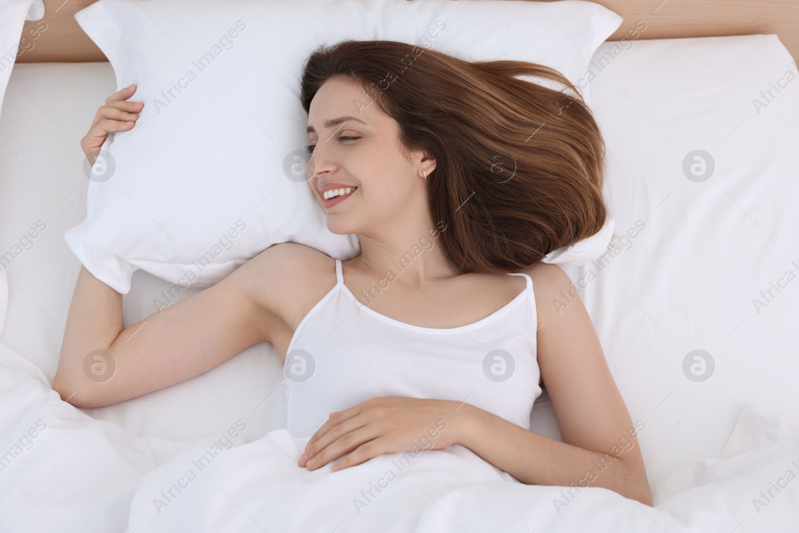 Photo of Bedtime. Happy woman lying in bed indoors, above view