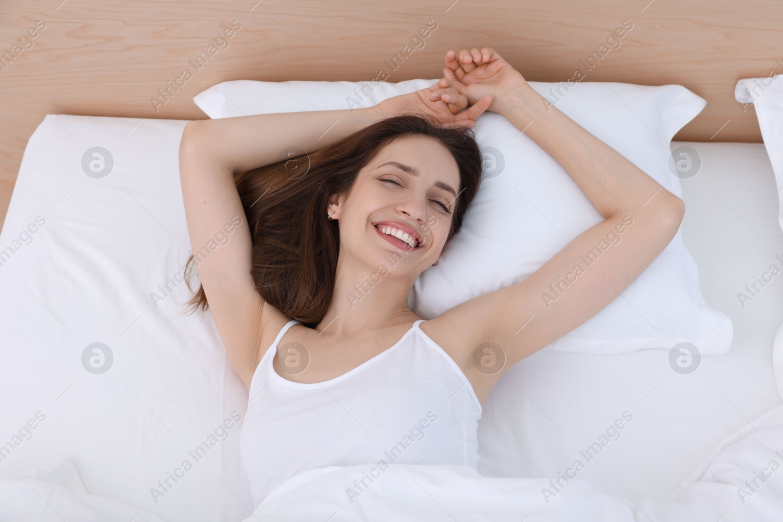 Photo of Bedtime. Happy woman lying in bed indoors, above view