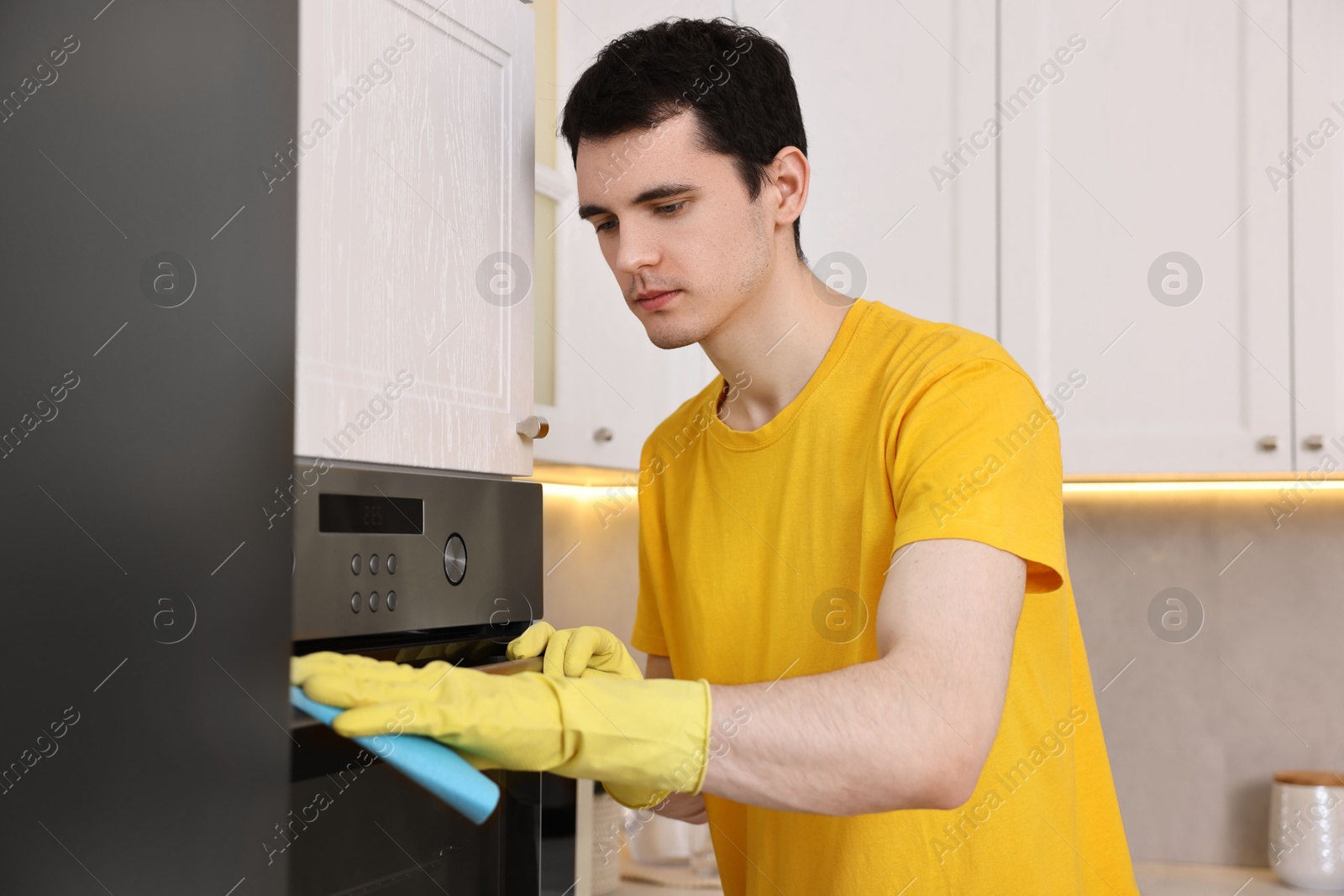 Photo of Professional janitor wearing uniform cleaning electric oven in kitchen