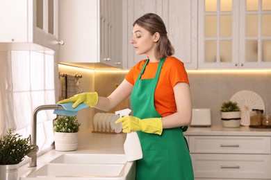 Photo of Professional janitor wearing uniform cleaning tap in kitchen