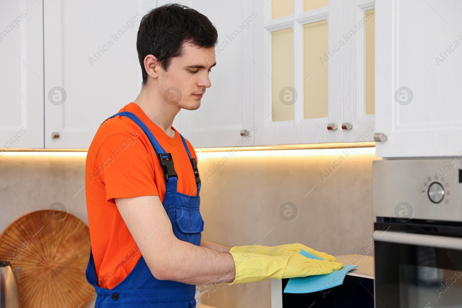 Photo of Professional janitor wearing uniform cleaning microwave oven in kitchen