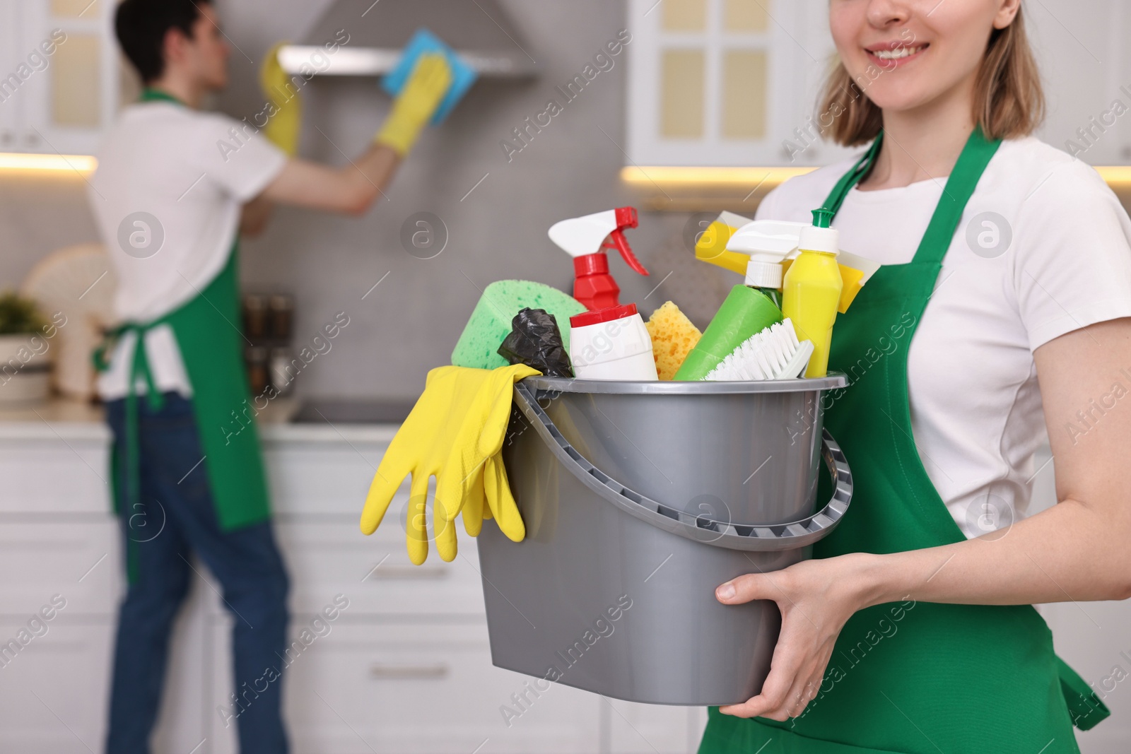 Photo of Cleaning service worker holding bucket with supplies in kitchen, closeup