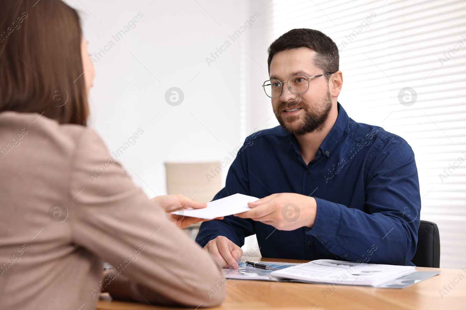 Photo of Boss giving salary in paper envelope to employee indoors