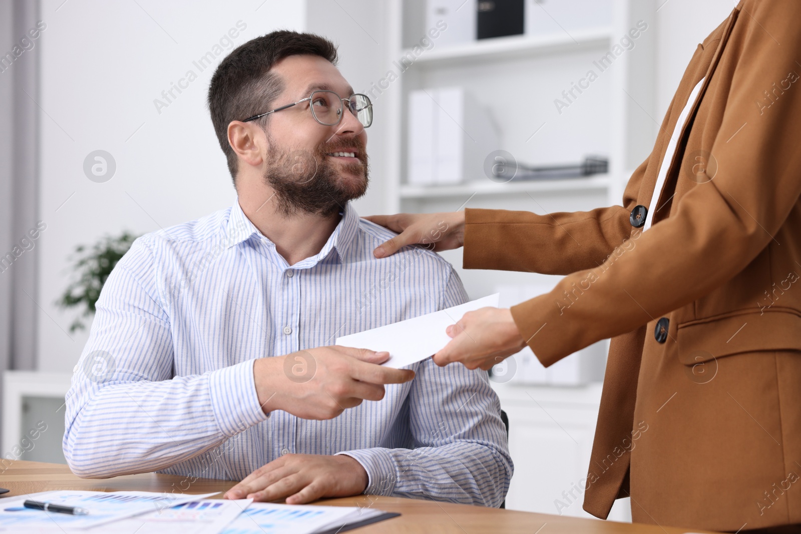 Photo of Boss giving salary in paper envelope to employee indoors