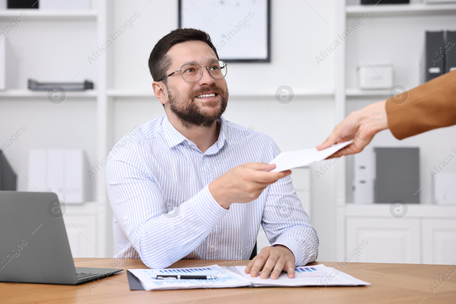 Photo of Boss giving salary in paper envelope to employee indoors