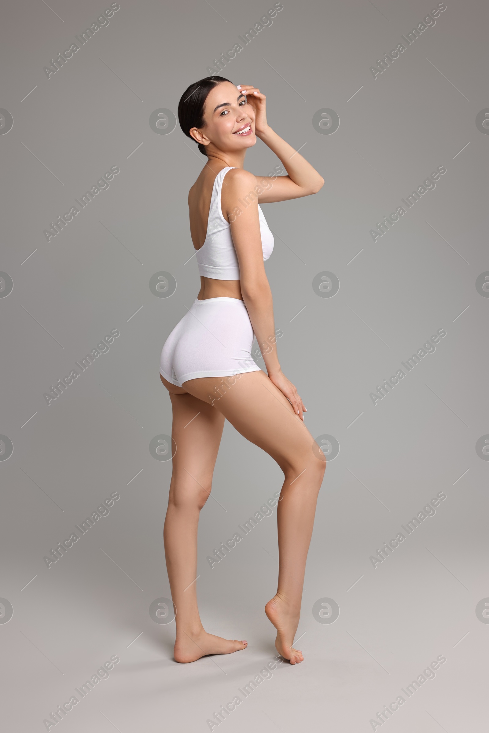 Photo of Smiling woman with perfect skin in underwear on grey background. Body care