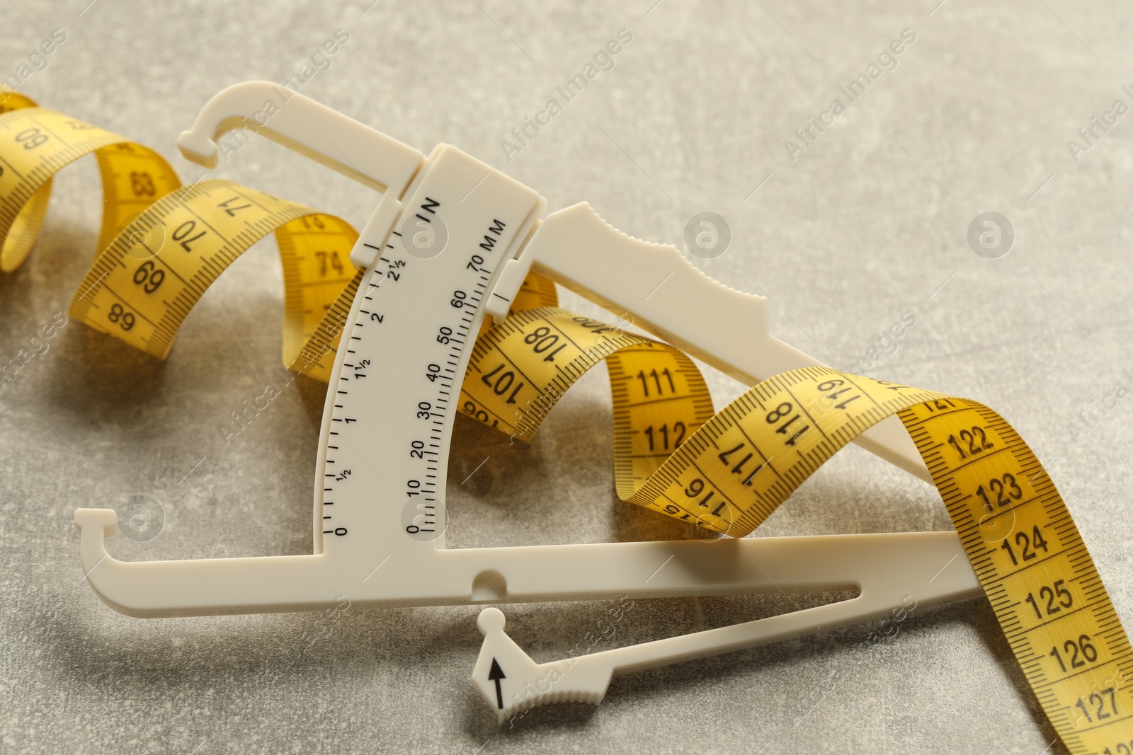 Photo of Plastic body fat caliper and measuring tape on light table, closeup