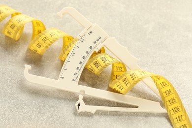 Photo of Plastic body fat caliper and measuring tape on light table, closeup