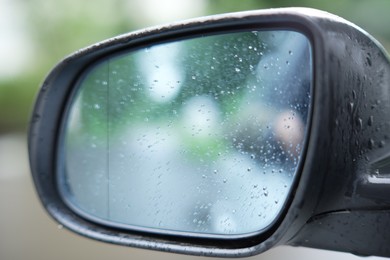 Photo of Car side view mirror with rain drops on blurred background, closeup