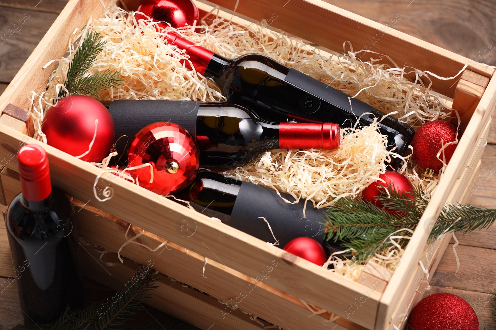 Photo of Wooden crate with bottles of wine, fir twigs and red Christmas balls on table