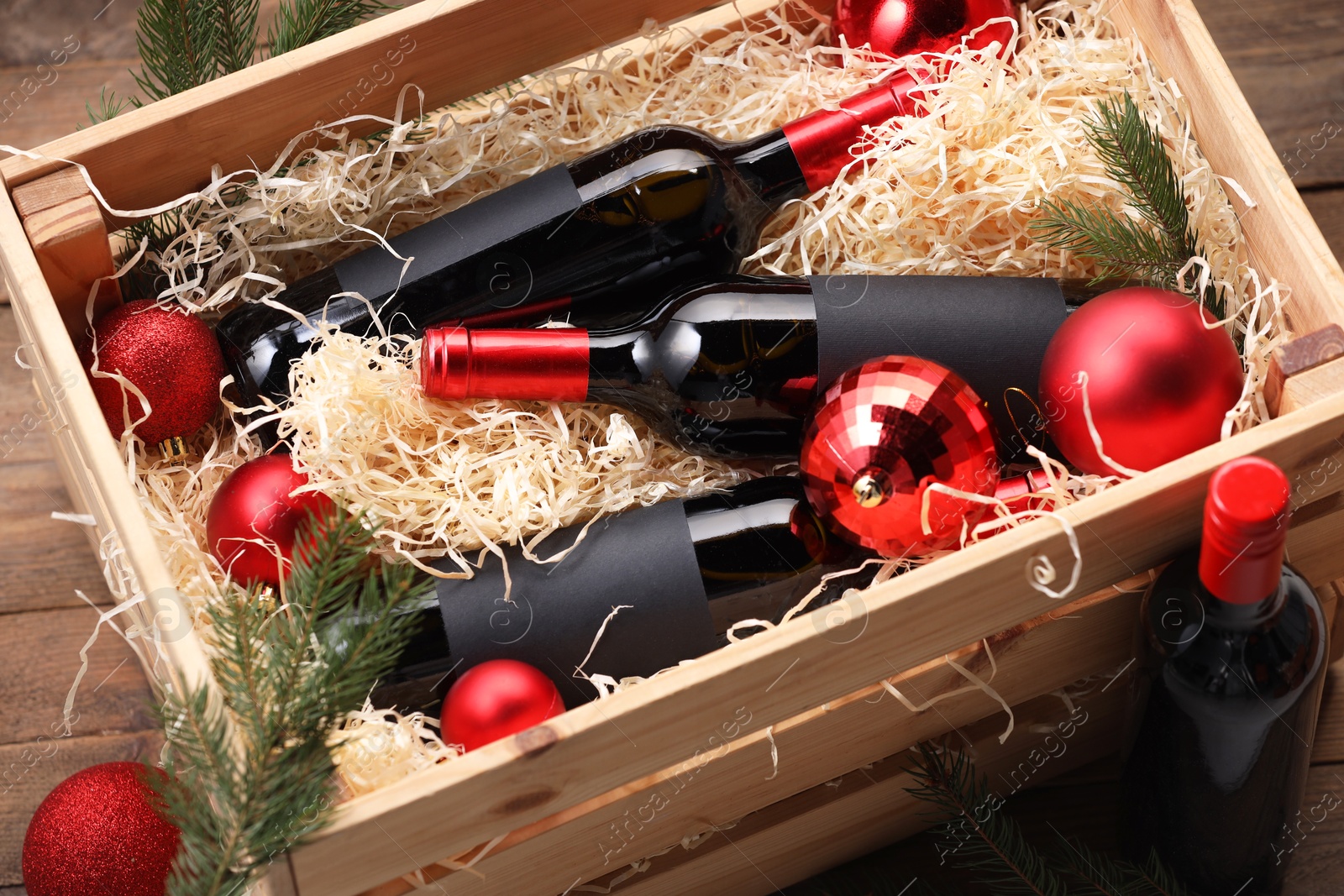 Photo of Wooden crate with bottles of wine, fir twigs and red Christmas balls on table