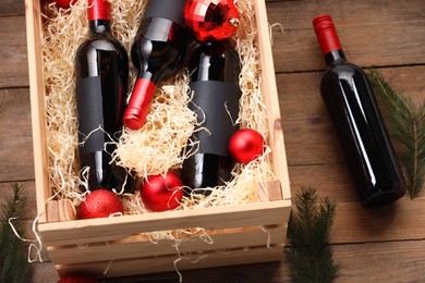 Photo of Wooden crate with bottles of wine, fir twigs and red Christmas balls on table, above view