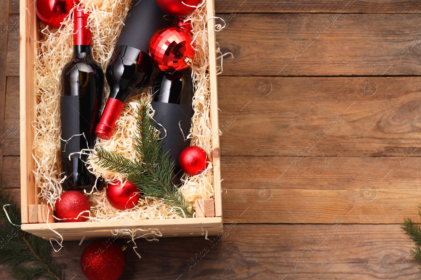 Photo of Wooden crate with bottles of wine, fir twigs and red Christmas balls on table, top view. Space for text