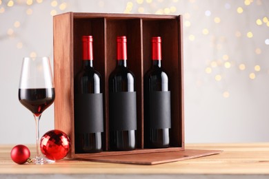 Photo of Wooden gift box with bottles of wine, glasses and red Christmas balls on table