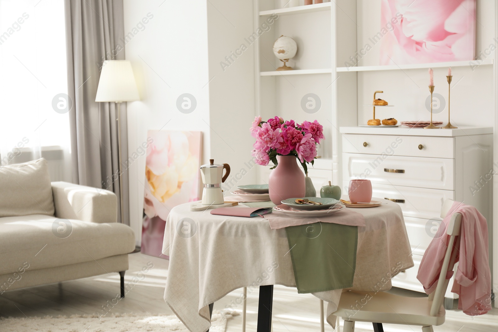 Photo of Pink peonies on table, chair and sofa in living room