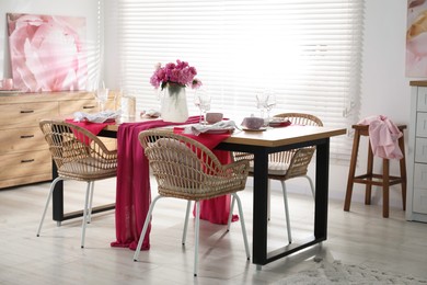 Photo of Pink peonies on table with beautiful setting and rattan chairs in dining room