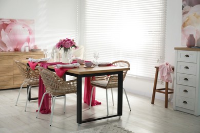 Photo of Pink peonies on table with beautiful setting and rattan chairs in dining room