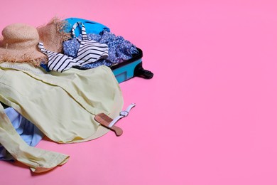 Photo of Open suitcase with traveler's belongings on pink background, space for text